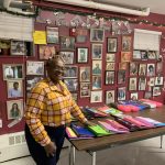 Photo of Sharon Curry in the Community Center. Pictures of inspirational people cover the walls and her student's notebooks fill the table. Happy Holidays.
